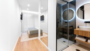 A modern bathroom with a glass shower enclosure, a round mirror, and a wooden vanity. - Casa D. Adelaide T1 (Azurara)