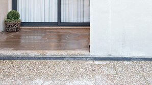 A modern building entrance with a concrete wall, a glass door, and a small potted plant. - Casa D. Adelaide T1 (Azurara)