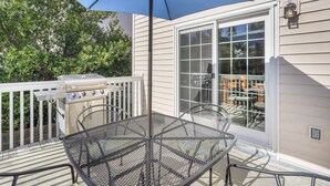 Une terrasse avec une table et des chaises en métal, un barbecue et un grand parasol.