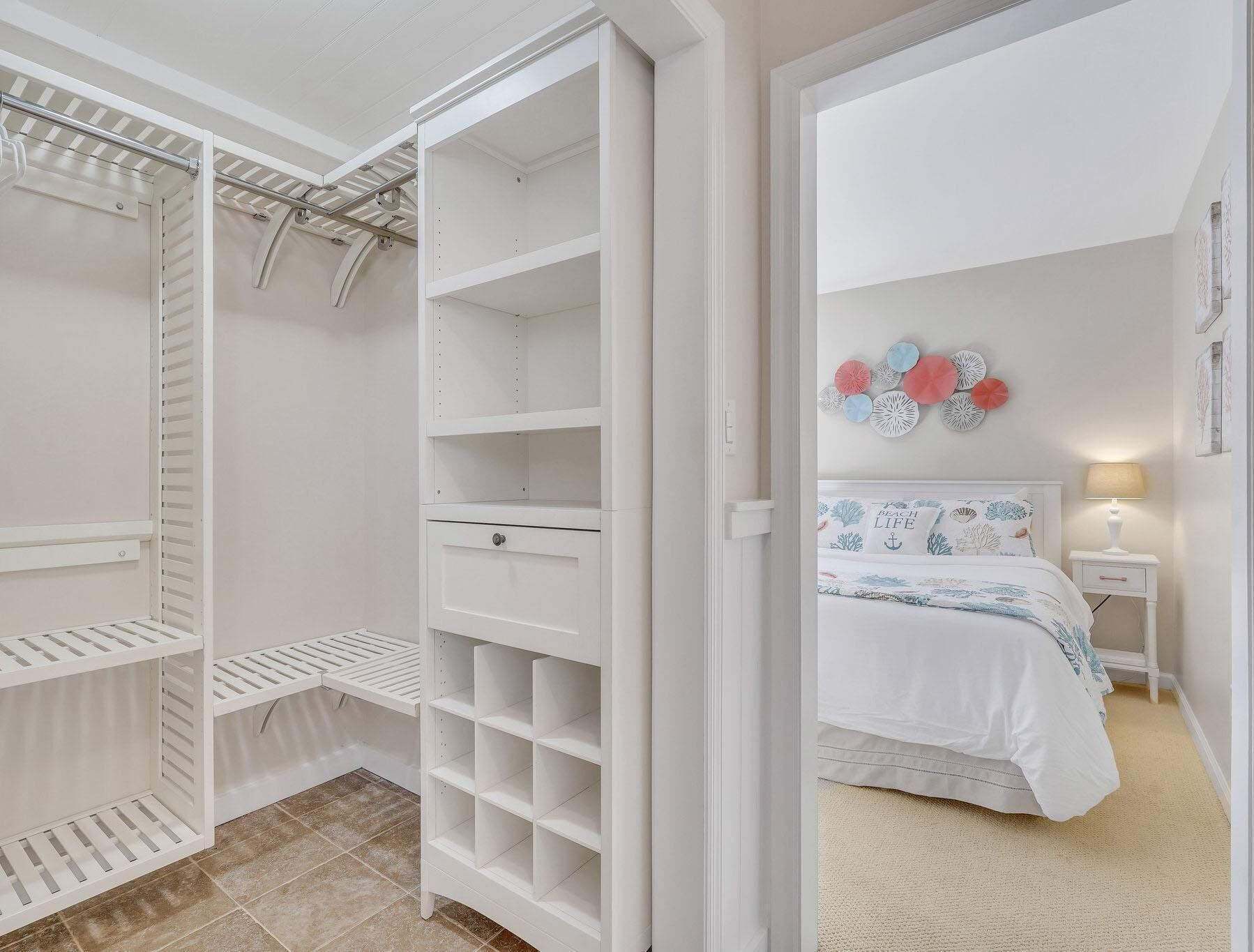Un dormitorio con cama, mesita de noche y armario blanco con varios estantes y cajones.