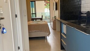 A hotel corridor with a bed, a bathroom, and a kitchen area. - Flat Nascente a passos do Mar (Ipojuca)