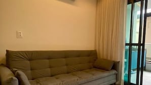 A modern living room with a sofa, an air conditioning unit, and a large window with curtains. - Flat Nascente a passos do Mar (Ipojuca)