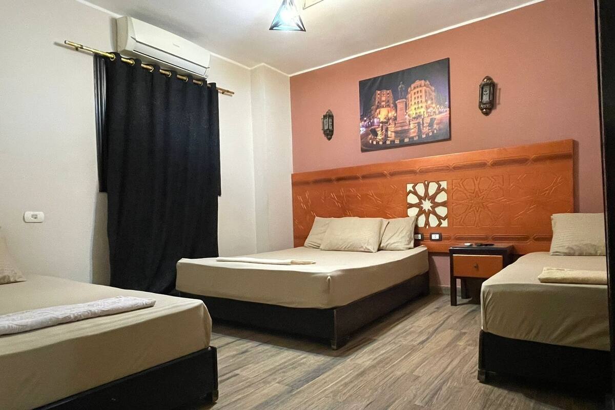 A hotel room with three beds, a wooden floor, a night sky mural, and a wall-mounted lamp.