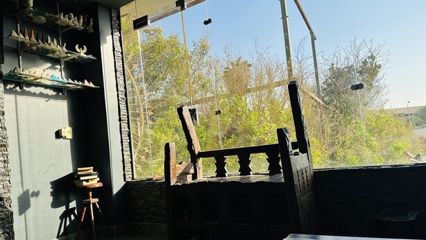 Ein Zimmer mit einem großen Fenster, einem Holzstuhl und Regalen mit verschiedenen Gegenständen.
