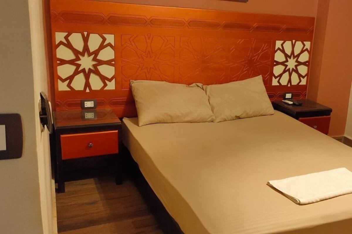 A hotel room with a bed, nightstands, and a red drawer unit.