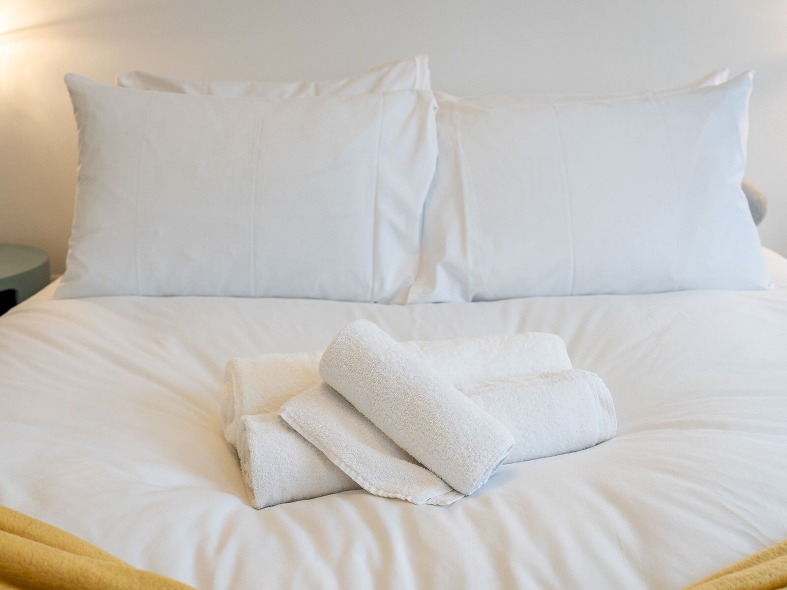 A neatly made bed with white linens and pillows, and a folded white towel on the bed.