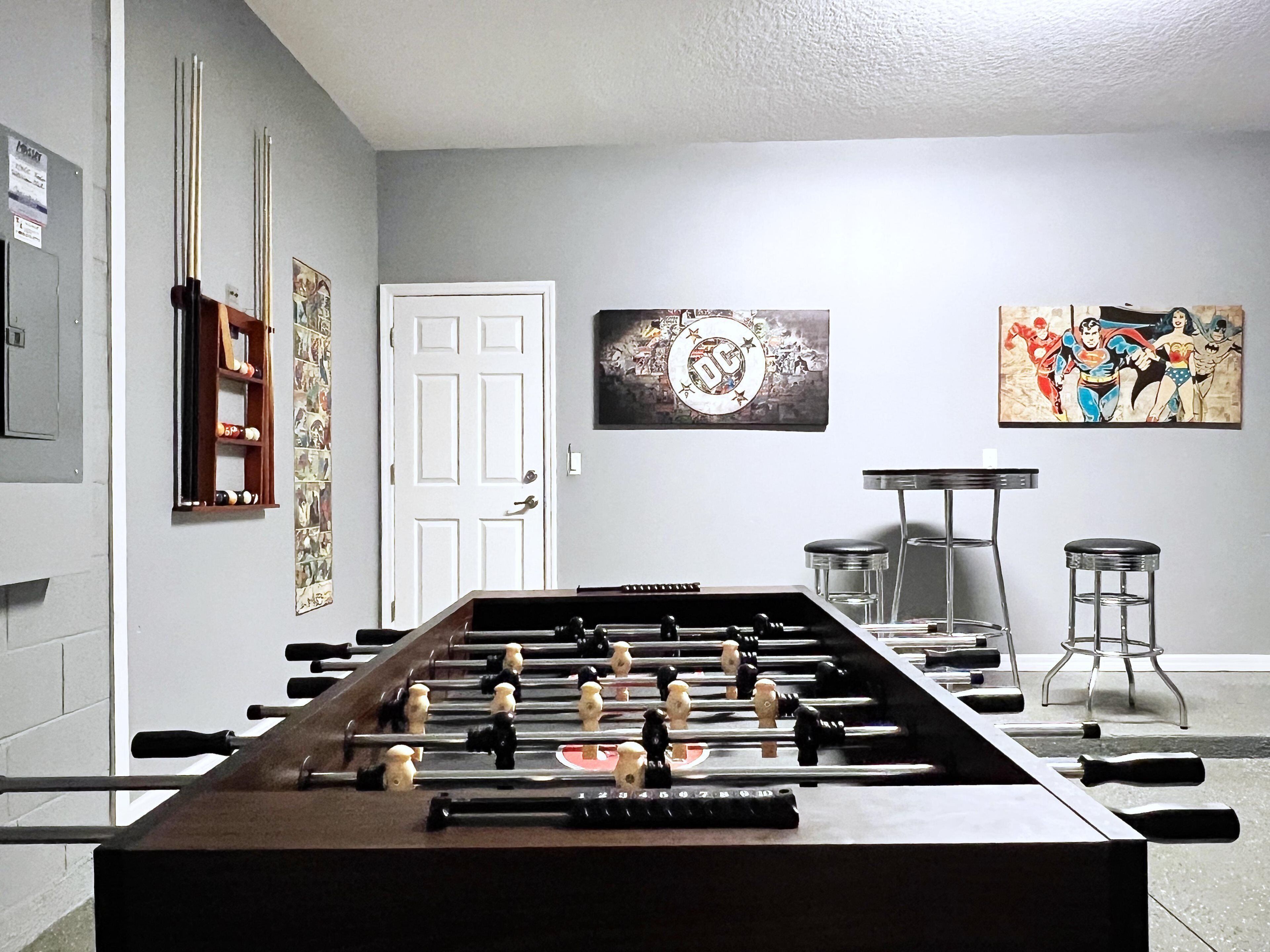 Una habitación con una mesa de fútbol de mesa, una puerta y dos cuadros en la pared.