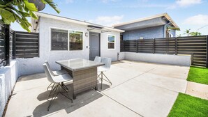 Eine moderne Terrasse mit Tisch aus Glas und weißen Stühlen, einem Betonboden und einem kleinen Gartenbereich mit Rasen.