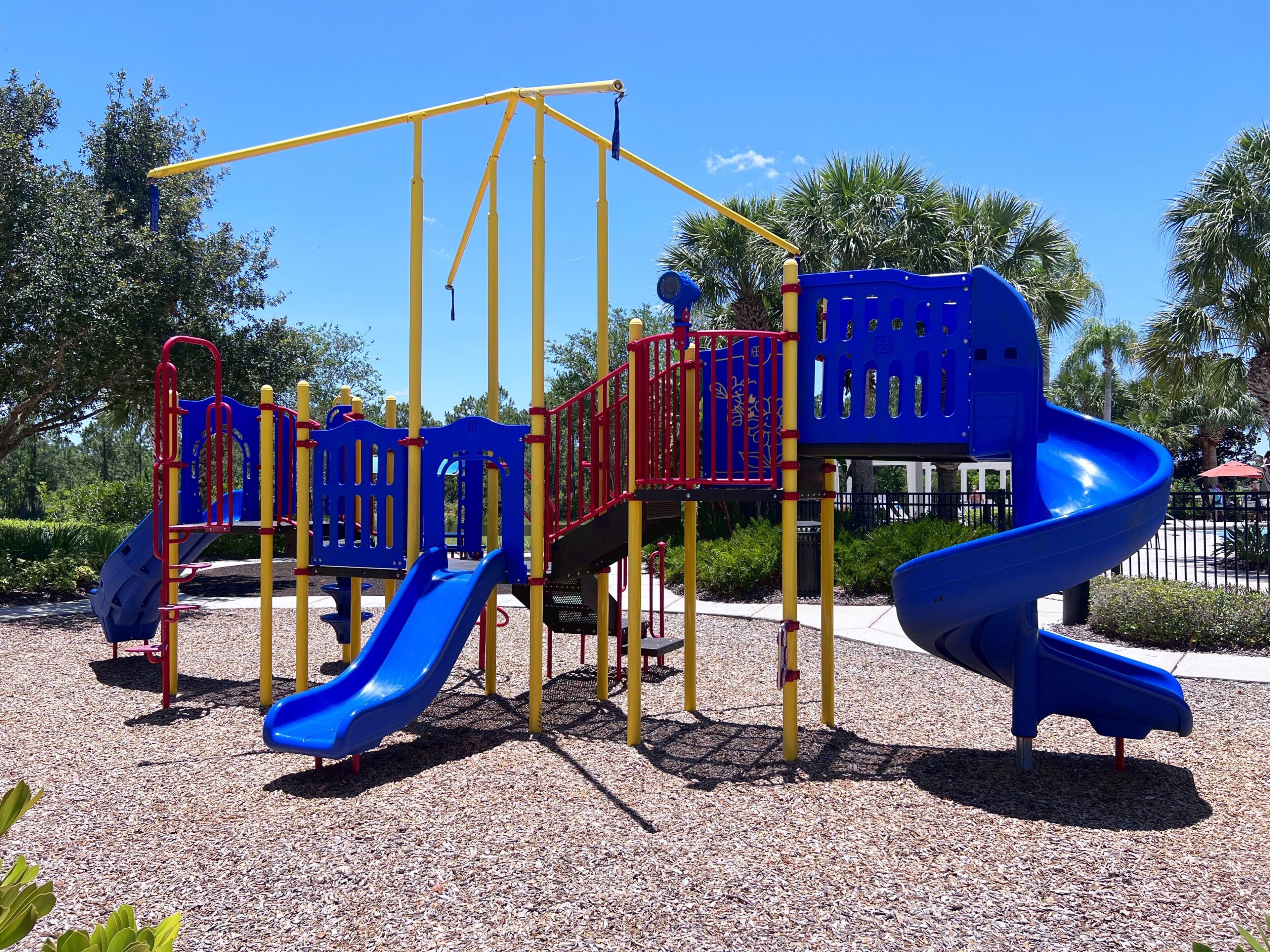 A playground with a blue slide, yellow and red climbing structures, and a blue spiral slide.