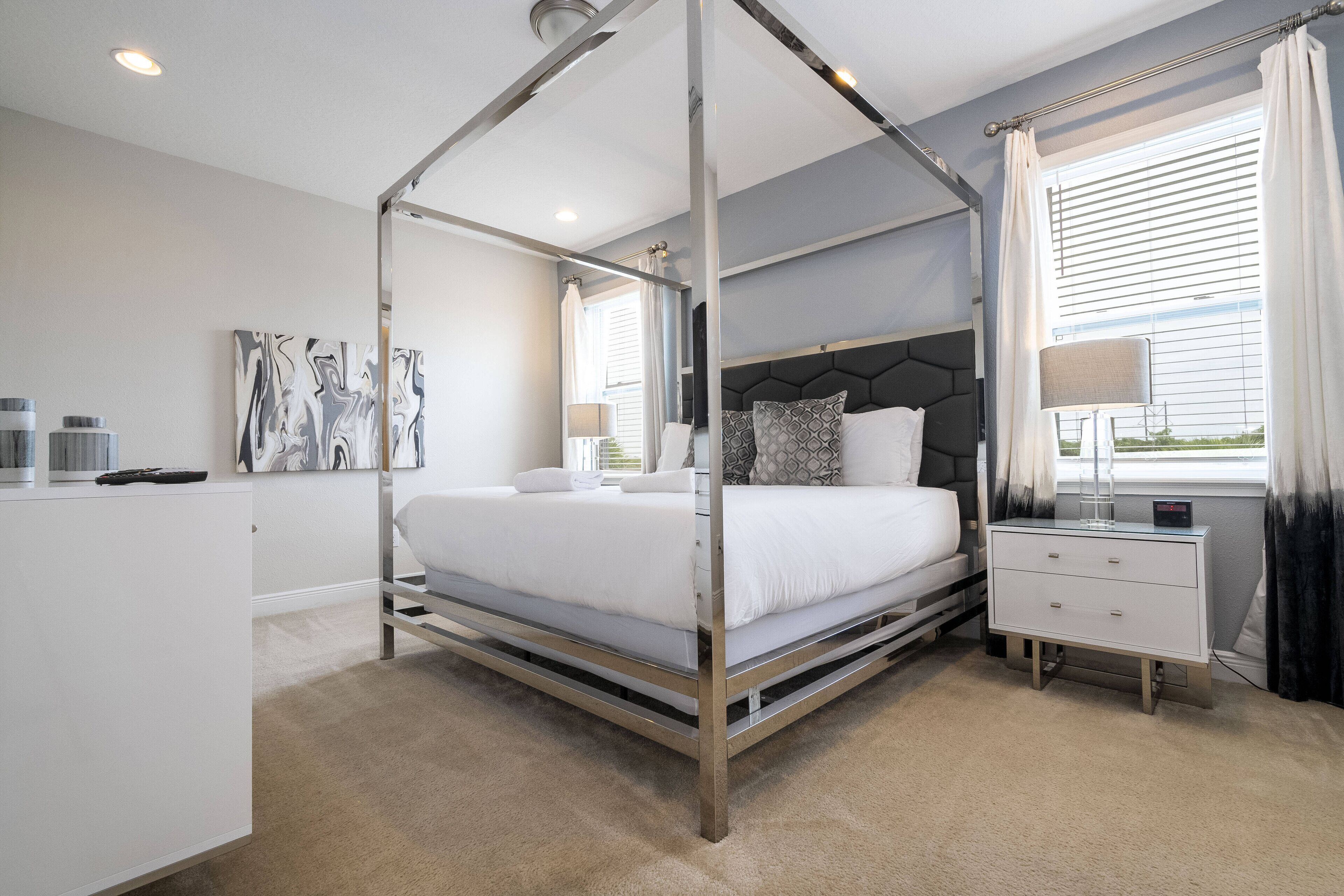 A modern bedroom with a four-poster bed, bedside tables, and a large window with curtains.