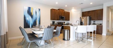 A modern kitchen with wooden cabinets, stainless steel appliances, and a dining area with grey chairs and a white table.