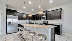 Una cocina moderna con armarios oscuros, electrodomésticos de acero inoxidable y una isla central con taburetes de bar.