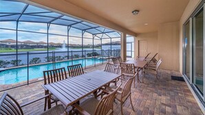 Un espacio al aire libre techado con piscina, mesa y sillas de madera, y vista al agua.