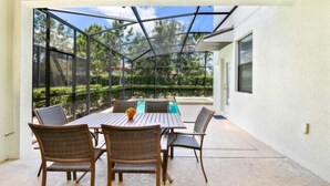 An outdoor patio with a table and chairs, a pool, and a view of the surrounding greenery.