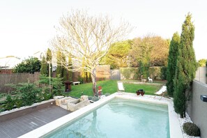 A backyard with a swimming pool, a wooden deck, and a fenced area with trees and shrubs. - Casa D. Adelaide T3 (Azurara)