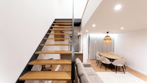 A modern interior with a wooden staircase, a dining area with a round table and chairs, and a sofa.