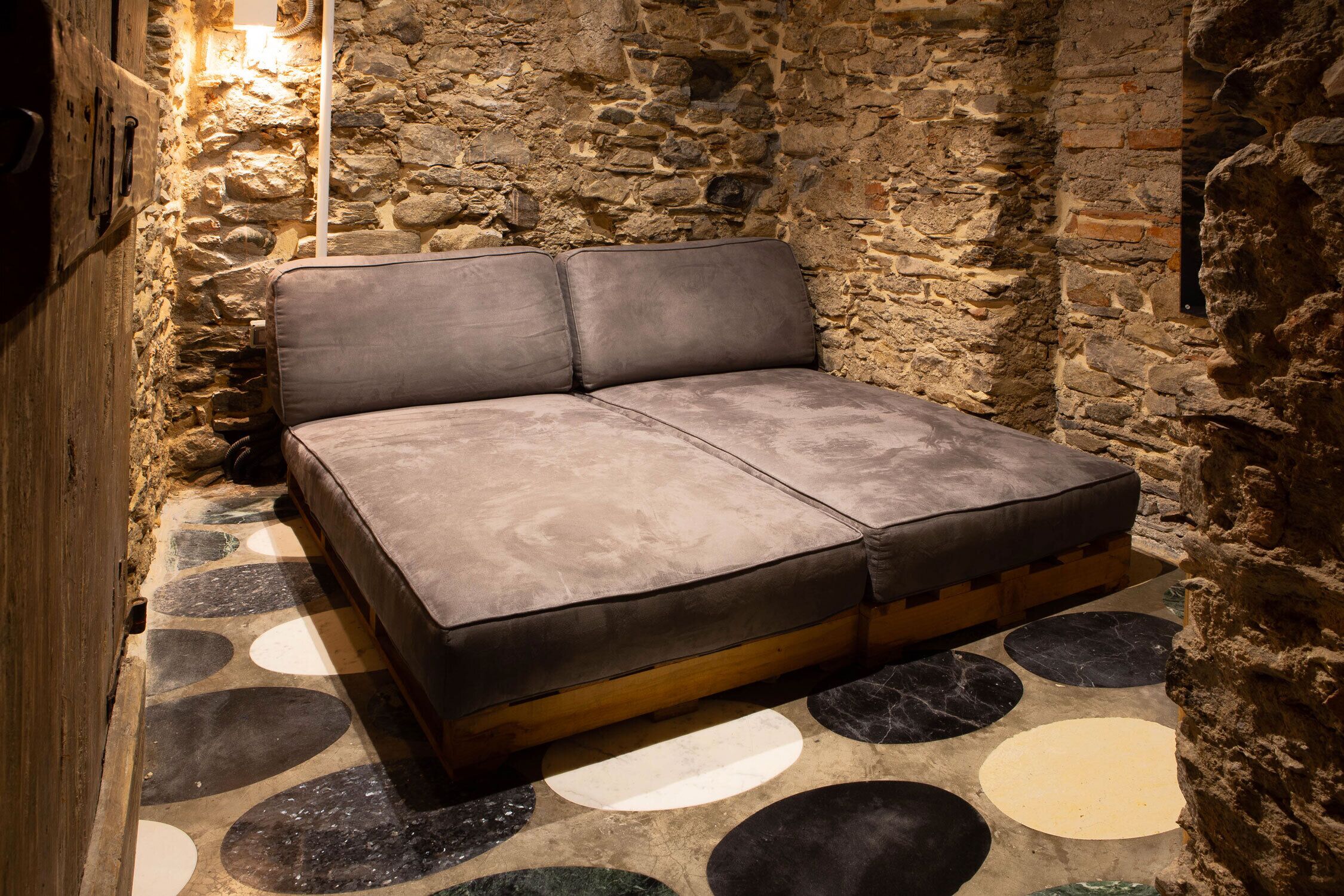 Un letto in una stanza dalle pareti in pietra e con pavimento decorato.
