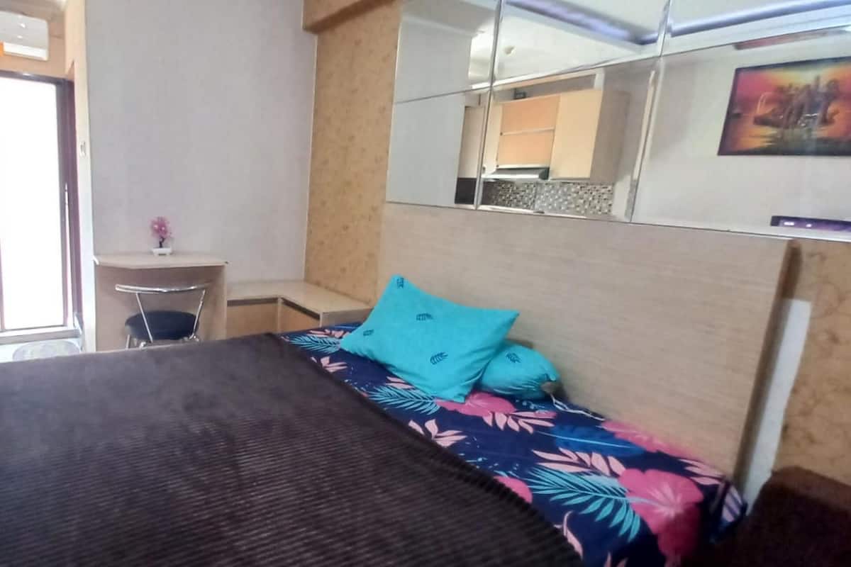 Quarto com cama, uma escrivaninha pequena, um espelho e janela.