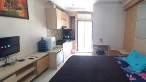 A compact hotel room with a bed, a TV, a small kitchenette, and a bathroom. - OYO 93480 Apartement Gateway Cicadas By Kelola Room (Bandung)
