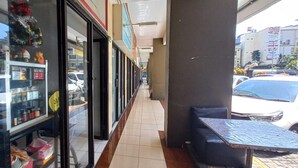A corridor with a storefront on the left, a tiled floor, and a table with chairs on the right. - OYO 93480 Apartement Gateway Cicadas By Kelola Room (Bandung)