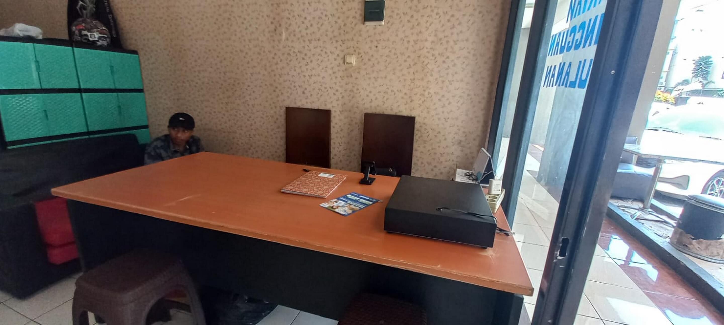 A reception desk with a large table, a black briefcase, and a magazine. There are two chairs and a green cabinet in the background.