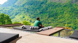 A man sitting on a deck with a view of a lush green mountain.