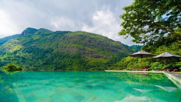 A clear pool with a view of a lush green hill and a gazebo with umbrellas.