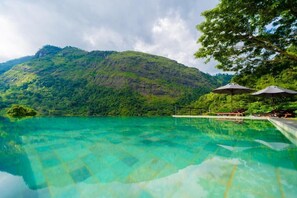 A clear pool with a view of a lush green hill and a gazebo with umbrellas. - Romantic Luxury Villa with a Mountain view (Nikapotha)