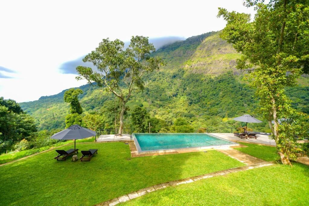 A swimming pool with lounge chairs and umbrellas, surrounded by lush greenery and hills.
