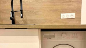 A compact washer and dryer unit with a wooden countertop and a modern faucet. - Appartement T2 - Proche Centre et Lac (Aix-les-Bains)