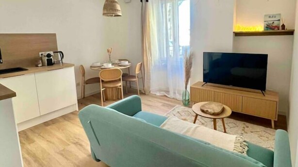 A modern living room with a sofa, a TV, a dining area, and a kitchen. - Appartement T2 - Proche Centre et Lac (Aix-les-Bains)