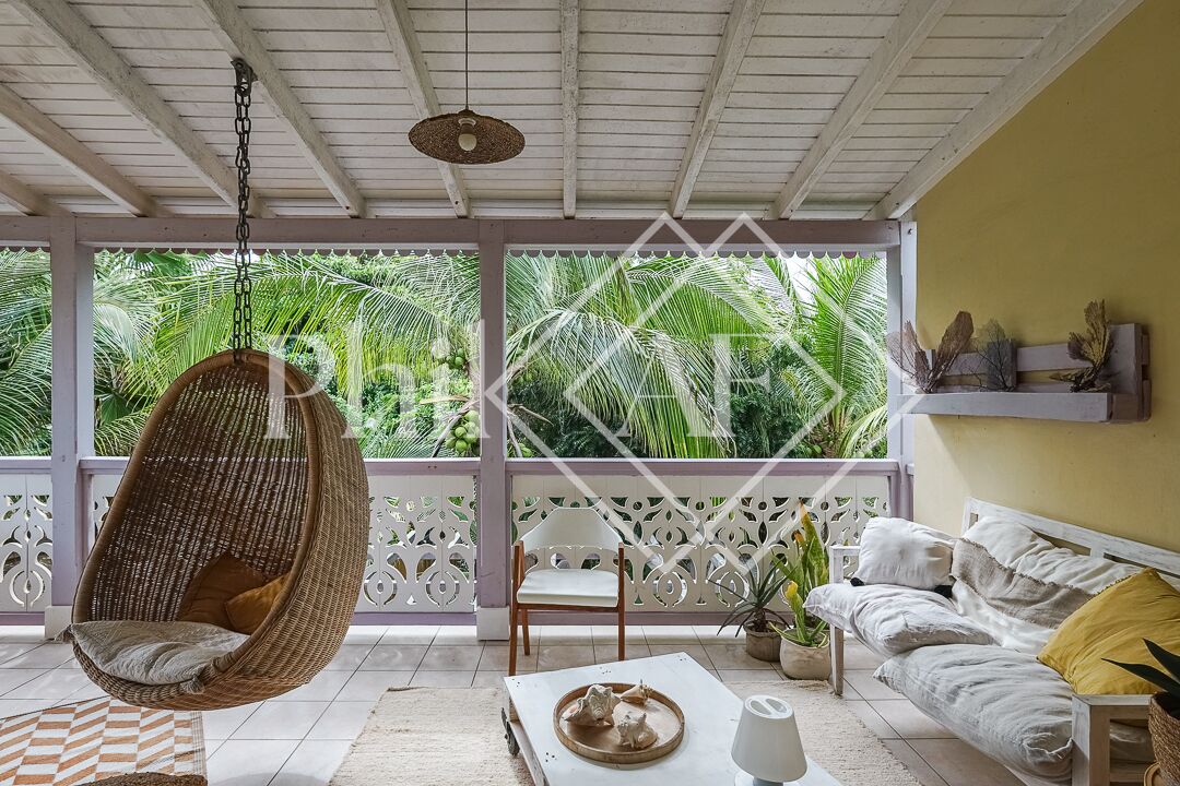 A room with a hanging chair, a sofa, a table with decorative items, and a view of lush greenery outside.
