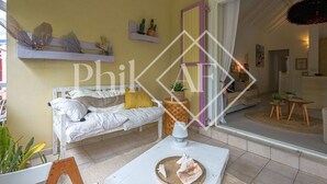 A cozy living room with a white sofa, a small table with a decorative shell, and a shelf with plants and a cactus.