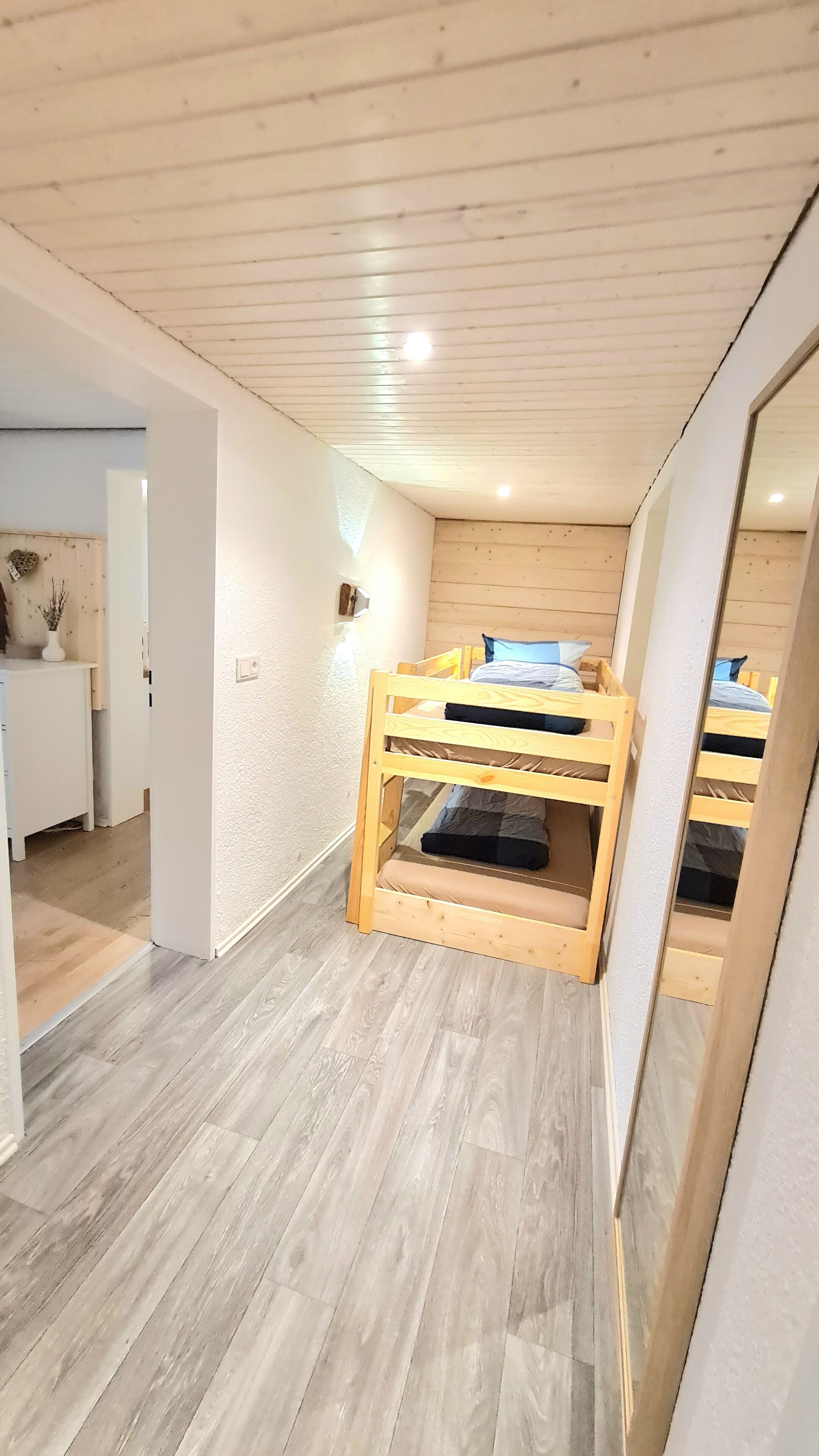 Une chambre avec un lit superposé, un bureau blanc et un miroir.