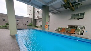 A swimming pool with a tiled edge, surrounded by a tiled floor. There are lounge chairs and a lifebuoy on the poolside. - Capital O 93481 Apartement Grand Asia Afrika By Kelola Room (Bandung)