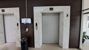 Two elevators, A01 and A02, in a modern lobby with marble walls and a trash bin. - Capital O 93481 Apartement Grand Asia Afrika By Kelola Room (Bandung)