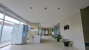 A hotel lobby with a reception desk, potted plants, and a large window. - Capital O 93481 Apartement Grand Asia Afrika By Kelola Room (Bandung)
