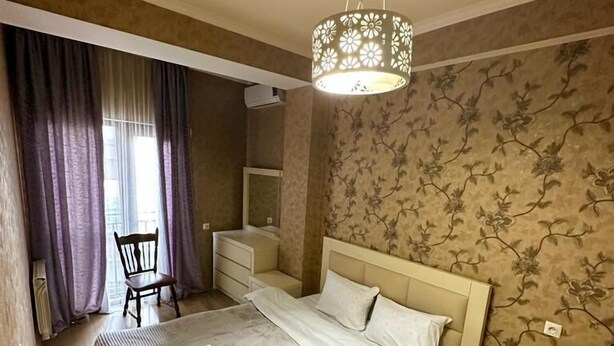 Ein Schlafzimmer mit Bett, Nachttischen, einem Sessel und einer Pendelleuchte.