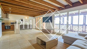 Een ruime woonkamer met houten plafond, een keuken op de achtergrond en een balkon met tuinmeubilair.