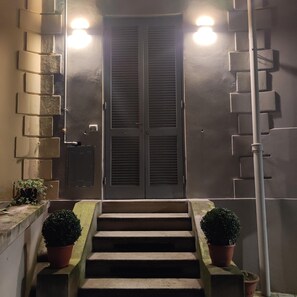 A set of concrete steps leading to a double door with a metal handle, flanked by two wall-mounted light fixtures. - Cozy studio apartment with small terrace (Milano)