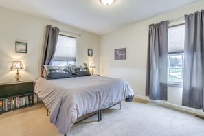 Ein Schlafzimmer mit einem Bett, zwei Nachttischlampen, einem Bücherregal und zwei mit Vorhängen versehenen Fenstern.