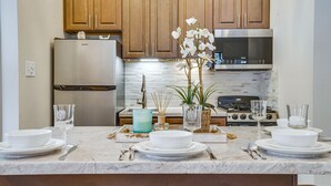 A kitchen with wooden cabinets, a stainless steel refrigerator, a stove, and a marble countertop with dining set. - Peaceful Ellsworth Vacation Rental w/ Grill (Ellsworth)
