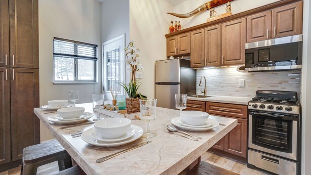 A modern kitchen with a marble countertop, stainless steel appliances, wooden cabinets, and a large island with dinnerware and glassware. - Peaceful Ellsworth Vacation Rental w/ Grill (Ellsworth)
