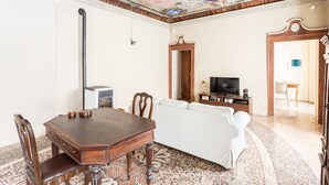 A dining area with a wooden table and chairs, a white sofa, and a television on a wooden cabinet. - PM3        (Castello Cabiaglio)