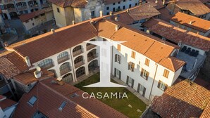 An aerial view of a building with a courtyard, surrounded by other buildings with red-tiled roofs. - PM3        (Castello Cabiaglio)