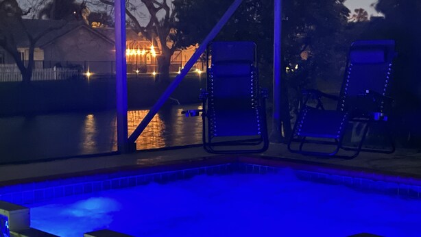 A swimming pool with blue lighting, two lounge chairs, and a view of a lit building across the water. - CASA BELLA - HEATED POOL- HOT TUB- POOL TABLE -BBQ-PEACEFUL OASIS- 4 BEDS-  (Boynton Beach)