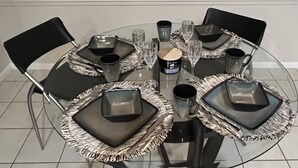 A round glass table with black chairs, square black plates, and clear wine glasses. - CASA BELLA - HEATED POOL- HOT TUB- POOL TABLE -BBQ-PEACEFUL OASIS- 4 BEDS-  (Boynton Beach)