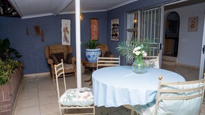 Une pièce comprenant une table ronde, deux chaises, un fauteuil en osier, une plante en pot et un vase avec des fleurs.