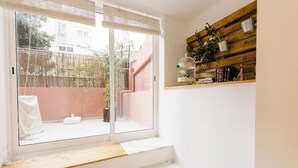 Et værelse med en skydedør af glas til en balkon, en træhylde med dekorative genstande og en hvid bænk.