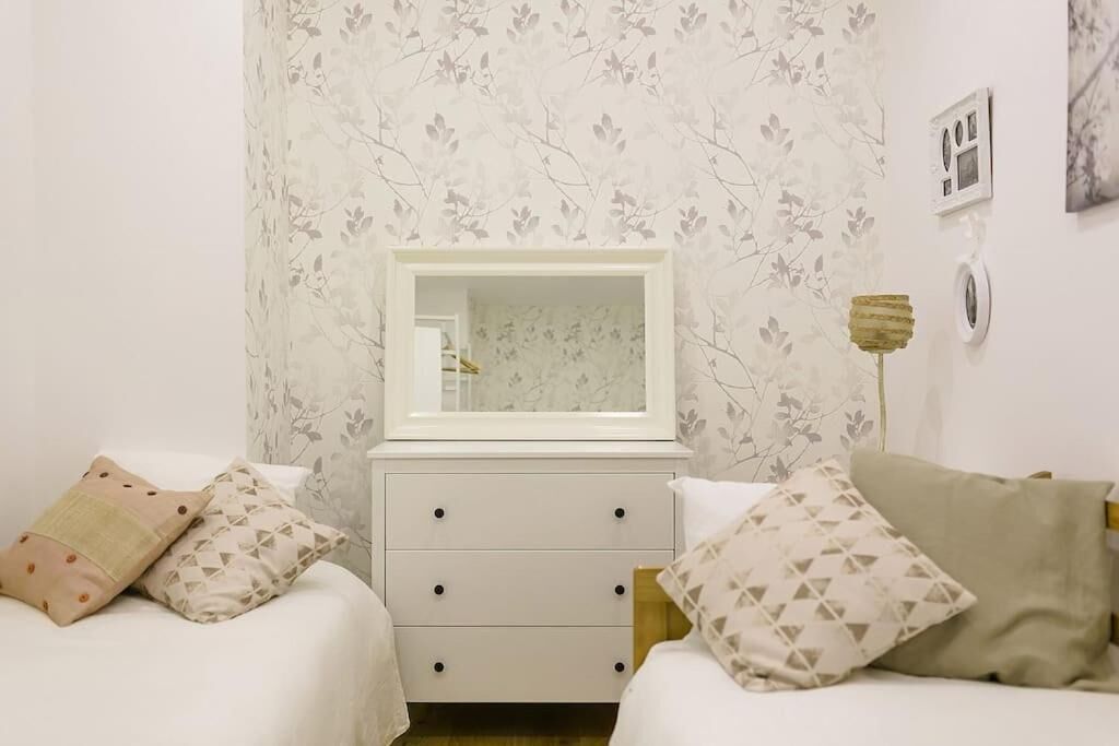 A bedroom with two beds, a nightstand, a mirror, and a wall-mounted light fixture.